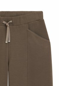 Bruine joggingsbroek met een elastische tailleband, trekkoord en een zijzak met contrasterende stikdetails. Zacht, gestructureerd materiaal.