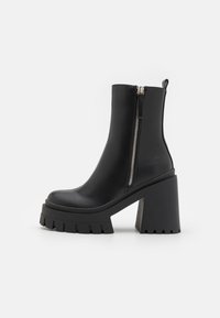 Bottines noires à talons, en cuir lisse, avec une semelle épaisse et un haut talon block, dotées d'une fermeture éclair et d'une languette pour un enfilage facile.