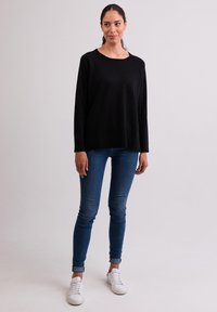 Schwarzer, übergroßer Pullover mit Rundhals und langen Ärmeln, kombiniert mit engen blauen Jeans und weißen Sneakers. Glatte Textur, lässiges Design.