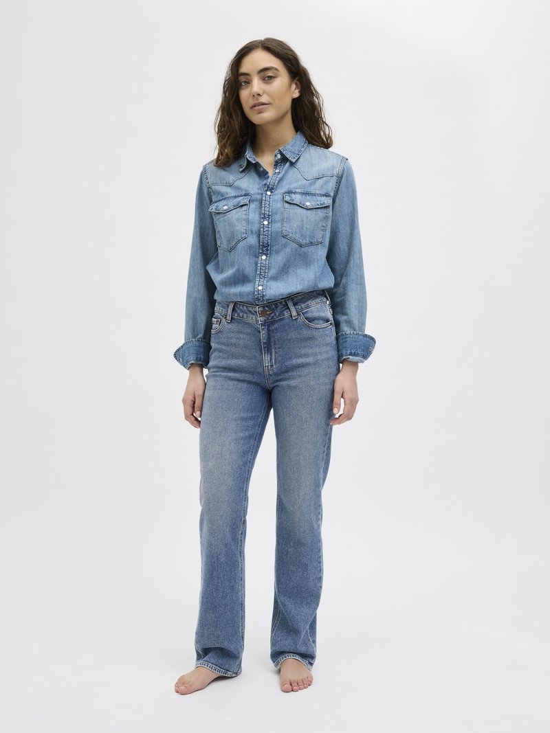 Ανοιχτό μπλε τζιν πουκάμισο με δύο τσέπες στο στήθος, σε συνδυασμό με ανοιχτό μπλε τζιν με ίσια γραμμή. Και τα δύο ρούχα διαθέτουν κλασικές λεπτομέρειες ραφής.