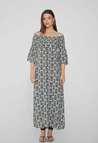 Vestido maxi negro y blanco con escote bardot, diseño estampado, mangas acampanadas y un corte suelto y fluido. Sandalias planas completan el look.
