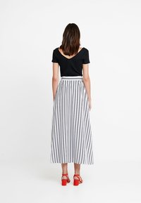 Black short-sleeve top paired with a white striped maxi skirt, featuring vertical black lines. The model wears red block-heel sandals.