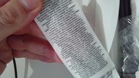Märke med skötselinstruktioner och materialkomposition: 88% polyester, 12% elastan, tryckt text på flera språk, vit tyg.