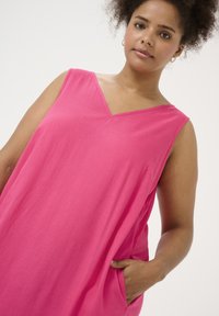 Vestido fucsia con cuello en V y diseño sin mangas. Tejido suave, corte relajado con bolsillos laterales. Textura lisa, adecuado para el uso casual.