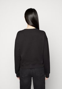 Sudadera negra corta hecha de tela suave, con escote redondo y costuras de hombro caídas, combinada con vaqueros oscuros de talle alto.