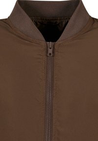 Chaqueta bomber marrón con un cuello alzado y una cremallera central. Está hecha de un material suave con un acabado mate y detalles de costura visibles.
