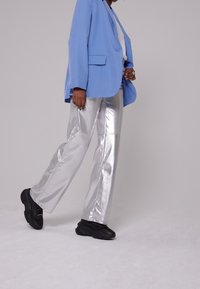 Blazer blu, top bianco, pantaloni larghi argentati lucidi e sneakers nere. Texture liscia, design sartoriale e colori a contrasto.