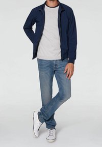 Marineblå bomberjakke med lynlås foran, grå T-shirt under, lys blå denimjeans og hvide sneakers med grå detaljer.