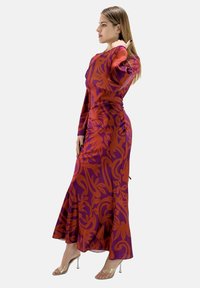 Långärmad, figurnära klänning i lila med stora orangea blommönster, med en utsvängd nederdel och silkeslen textur. Genomskinliga klacksandaler.
