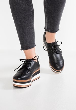 Sorte læderplateaustøvler med perforeret design og snørebånd; hvid og brunstribet sål; elegant, rundet tå; båret med mørkt denim.