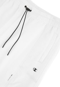 Shorts de sport blancs avec une taille élastique et un cordon de serrage noir. Comprend des poches latérales et un petit logo noir sur l'ourlet inférieur.