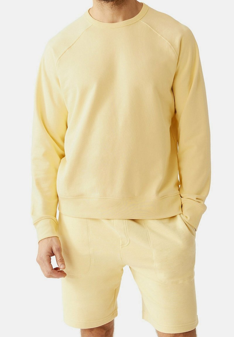 Felpa di cotone gialla con maniche lunghe, colletto e orlo a coste, abbinata a pantaloni corti coordinati con tasche laterali e una texture liscia.