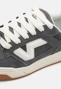 Baskets en daim gris avec accents blancs, présentant un bout arrondi, des lacets blancs épais et une semelle en caoutchouc clair. Détails perforés sur les côtés.