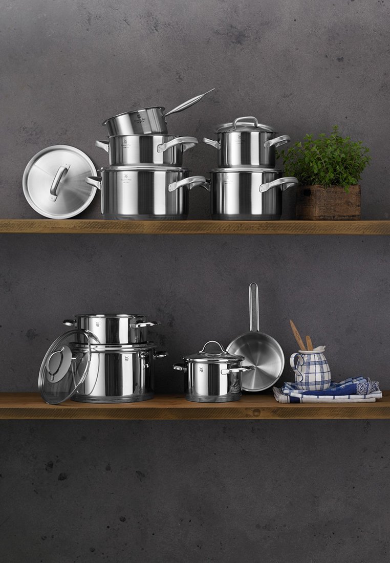 Zestaw garnków ze stali nierdzewnej na drewnianej półce, w tym garnki, patelnie, pokrywki i przybory kuchenne. Posiada wypolerowane powierzchnie i uchwyty.
