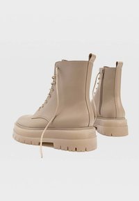 Botas de tobillo beige hechas de piel suave, con una suela de plataforma gruesa, cierre de cordones en la parte delantera y una cremallera lateral adicional para facilitar el uso.