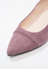 Chaussure plate en daim lavande à bout pointu avec un détail de bordure festonnée sur le devant et une doublure intérieure beige.