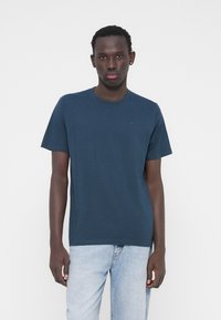 Tamsiai mėlynas medvilninis marškinėlis, pagamintas iš minkštos medvilnės, su užapvalintu kaklu ir trumpomis rankovėmis. Paprastas dizainas su mažos logotipu ant krūtinės.