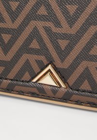 Portefeuille texturé marron avec motif géométrique en marron foncé. Équipé de quincaillerie triangulaire dorée et de coutures noires le long des bords.