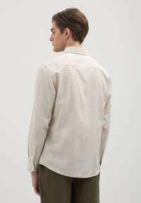 Hellbeige Langarmhemd mit Kragen, strukturiertem Stoff und geknöpften Manschetten. Es hat einen geraden Saum und dezente Nahtdetails.