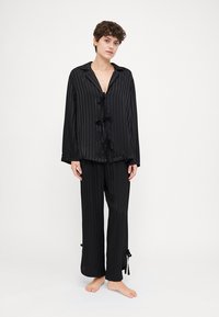 Conjunto de pijama a rayas negras en una tela suave, que incluye una parte superior con cuello y cierres de lazo, y pantalones a juego con tiras ajustables en el dobladillo.