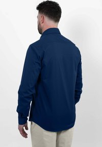 Marineblauwe langekraagshirt met een button-down kraag, gladde textuur en afgeronde zoom. De stof lijkt lichtgewicht en iets getailleerd.