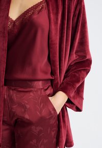 Ensemble bordeaux composé d'un kimono en velours, d'un caraco orné de dentelle et d'un pantalon à motifs. Texture lisse avec des accents floraux.