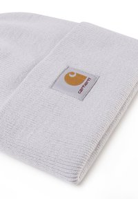 Gorro de punto blanco con vuelta. Presenta una etiqueta de Carhartt con un logo amarillo sobre un fondo blanco. Tejido texturizado.