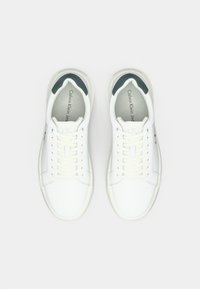 Une paire de baskets blanches basses Calvin Klein avec des lacets et des collines de talon rembourrées gris-noir, vues de dessus sur fond blanc.
