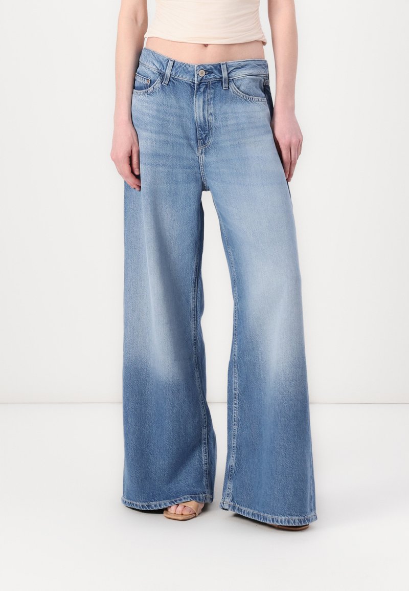 Jeans de denim de pierna ancha en azul claro, con una cintura alta, detalles de desvanecimiento y un diseño clásico de cinco bolsillos con cierre de botón.