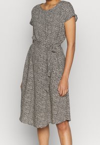 Vestido floral en blanco y negro con mangas cortas, cintura ceñida y falda a la altura de la rodilla; presenta un escote redondo y una cinta de tela.