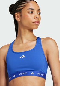 Blue sports bra with a smooth texture, wide straps, and a white logo. The band features "TECHFIT" in contrasting blue. Rounded neckline.