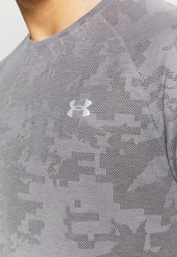Camisa deportiva gris hecha de tejido con patrón, que presenta un diseño sutil y un pequeño logo en plata reflectante en el área del pecho.
