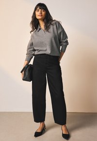 Grå strikpullover med krave, kombineret med højttaljede sorte bukser med vide ben. Sort lædertaske og sorte slingback-sko.