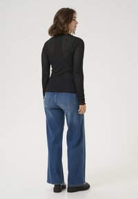 Haut noir à manches longues avec un motif texturé, associé à un jean large à taille haute bleu et des chaussures à plateforme noires.