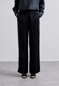 Svarta vida byxor med elastisk midja, med två sidofickor och ett mjukt, lätt tyg. Tillsammans med öppna sandaler.