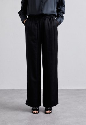 Svarta vida byxor med elastisk midja, med två sidofickor och ett mjukt, lätt tyg. Tillsammans med öppna sandaler.