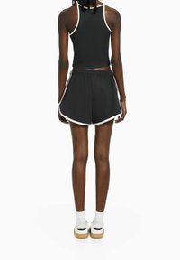 Svart atletisk crop top med vit kant, kombinerad med svarta shorts som har vita detaljer och en avslappnad passform. Vita sneakers med plattformssula.