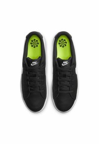 Sneakers in pelle nera con suole bianche, dotati di lacci neri e un'intersuola verde brillante con un motivo floreale. Logo Nike sulla linguetta.