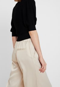 Černý pletený svetr s nabíranými rukávy a žebrovanými manžetami, spárovaný s béžovými širokými kalhotami s elastickým páskem a zadními kapsami.