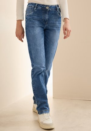Jean en denim bleu clair avec une coupe droite, présentant un design classique à cinq poches et une légère décoloration. Associé à des baskets blanches.