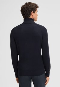 Marineblau gerippter Pullover mit hohem Kragen, langen Ärmeln und figurbetontem Design; strukturiertem Stoff mit dezentem Stretch für mehr Komfort.
