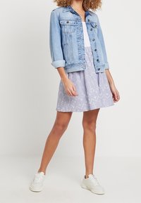 Denim jacket, light blue, with rolled sleeves and two chest pockets; white top underneath; purple skirt with white floral patterns; white sneakers.