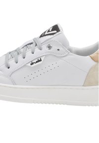 Zapatilla de cuero blanca con cordones grises, perforaciones en el lateral, una lengüeta de talón de ante beige claro y una suela de goma blanca sólida. Acento de logo negro.