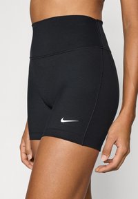 Μαύρα αθλητικά σορτς με ψηλή μέση και ομαλή υφή, με λευκό λογότυπο Nike στο πλάι. Διαθέτουν ελαστική ζώνη μέσης και εφαρμοστή σχεδίαση.