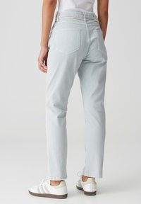 Jeans en denim bleu clair avec une coupe droite, dotés de deux poches arrière et d'une taille avec un détail de passant de ceinture contrastant. Assortis à des baskets blanches.