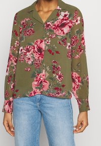 Blusa floreale verde con fiori rosa e rossi, maniche lunghe, chiusura a bottone e colletto. Realizzata in tessuto leggero con una vestibilità comoda.
