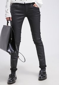 Svarta slim-fit läderbyxor med en slät yta, tillsammans med en svart väska och svarta flata skor, under en ljus mönstrad tröja.