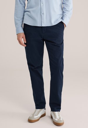 Marineblauwe katoenen chino's gecombineerd met een lichtblauw overhemd met knopen en witte sneakers met grijze accenten en rubberen zolen.