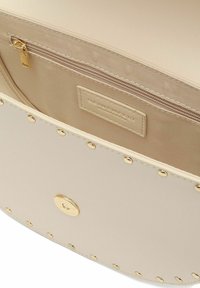 Borsa beige con un'esterno liscio e borchie dorate. L'interno presenta una tasca con zip, fodera beige e un'etichetta del marchio.