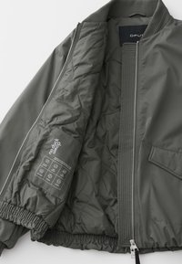 Green quilted jacket with zipper partially open, showing inner pocket labeled "no duck muop" and elastic cuffs and hem.